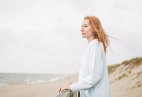 retrato de jovem ruiva de suéter azul claro na praia de areia à beira-mar em tempestade foto