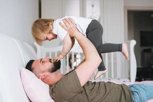 feliz pai jovem e menina filha se divertindo na cama em casa foto