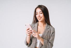 jovem mulher de negócios asiáticos feliz com cabelos longos de terno usando telefone celular em fundo cinza foto