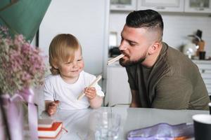 jovem pai feliz alimentando e se divertindo com a filhinha na cozinha em casa foto