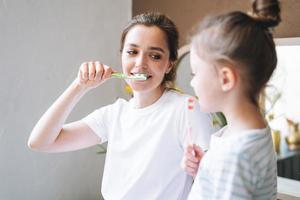 jovem mãe mulher com cabelo comprido com filha adolescente de pijama escovando os dentes de manhã em casa foto
