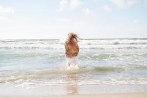 jovem mulher bonita com cabelo comprido na camisola bege curtindo a vida na praia do mar no pôr do sol foto