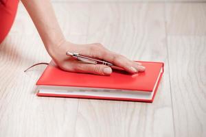 close-up da mão de uma jovem com uma caneta e um caderno para escrever o plano do dia. o conceito de trabalhar e estudar em casa. foto