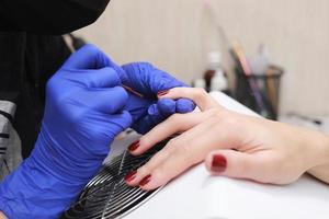 mestre em luvas de proteção durante uma manicure no salão de beleza. mestre manicure enverniza o gel marsala nas unhas de uma cliente do sexo feminino. o conceito de beleza e saúde. foto