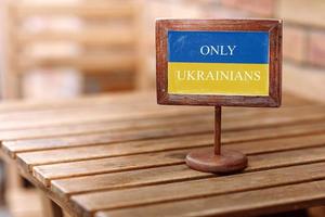 prato reservado de madeira vazio na mesa de madeira em um restaurante com texto para café convidados apenas povo ucraniano com cores bandeira da ucrânia azul e amarelo foto