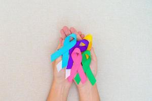 dia mundial do câncer, 4 de fevereiro. mão segurando fitas azuis, vermelhas, azul-petróleo, brancas, rosa, roxas e amarelas para apoiar pessoas vivas e doentes. conceito de dia de conscientização de saúde e autismo foto