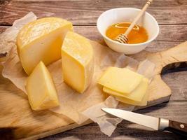 queijo duro artesanal. queijo de fazenda natural em uma velha tábua de madeira com mel em uma xícara foto