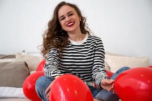 closeup de uma jovem segurando um balão vermelho em forma de coração enquanto está sentado na cama. celebração do dia dos namorados, aniversário ou dia da mulher. foto