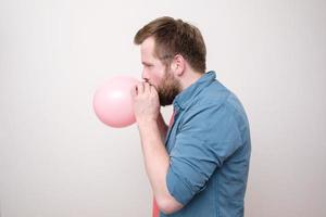 perfil de um homem caucasiano inflando um balão rosa. preparação para o feriado. fundo branco. foto