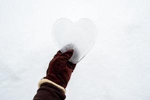 coração, símbolo do amor, feito de gelo, é segurado por uma mão em luvas quentes de camurça marrom. Dia dos Namorados. conceito romântico. copie o espaço. foto