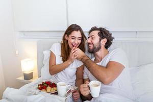 casal apaixonado tomando café da manhã na cama. jovem casal caucasiano tomando café da manhã romântico na cama. feminino e masculino, duas xícaras de café, frutas e biscoitos coloridos. foto