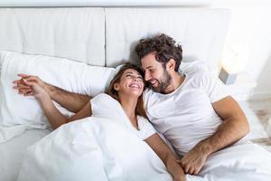 jovem casal apaixonado na cama. jovem casal deitado na cama e rindo enquanto faz cócegas um no outro. feliz casal jovem sensual deitado na cama juntos pela manhã foto