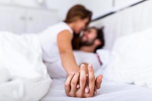 casal romântico na cama desfrutando de preliminares sensuais. concentre-se nas mãos de homem e mulher. feliz casal jovem sensual deitado na cama juntos. lindo casal apaixonado beijando na cama. foto