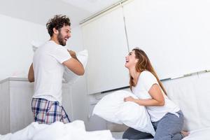 casal se divertindo enquanto luta de travesseiros. jovem casal feliz bateu os travesseiros na cama em um quarto em casa. foto