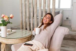 xícara de chá, café e frio. mulher deitada no sofá tomando café quente e curtindo a manhã, estando sonhadora e relaxada. menina coberta de cobertor faz pausa em casa foto