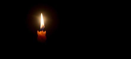 uma única chama de vela acesa ou luz brilhando em uma bela vela espiral laranja no espaço de cópia de fundo preto ou escuro para adicionar texto na mesa na igreja para o natal, funeral ou serviço memorial foto