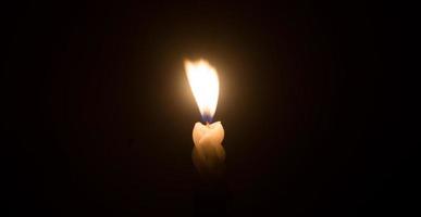 uma única chama de vela acesa ou luz brilhando em uma vela branca em espiral contra um pequeno vento soprando em fundo preto ou escuro na mesa na igreja para o natal, funeral ou serviço memorial foto