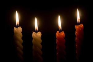 chamas de velas acesas ou luzes brilhando em três velas espirais brancas e laranja em fundo preto ou escuro na mesa na igreja para o natal, funeral ou serviço memorial foto