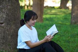 mulher asiática sentada com as costas contra uma árvore lendo um livro. conceito. mulher asiática fazendo atividades ao ar livre, como ler livros, trabalhar, fazer um piquenique com a família. foco suave e seletivo foto