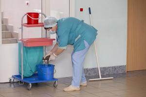 uma faxineira adulta de uniforme limpa o corredor do hospital. foto
