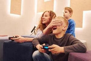 crianças alegres sentadas dentro de casa e jogando videogame juntos foto