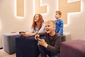 crianças alegres sentadas dentro de casa e jogando videogame juntos