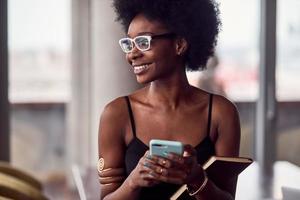 alegre mulher afro-americana segurando smartphone e bloco de notas foto