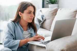 mulher jovem e bonita em jeans e camisa azul, deitada no sofá com o laptop foto