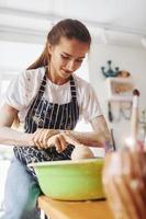 jovem ceramista feminina trabalhando usando roda de oleiro dentro de casa e fazendo produtos de argila feitos à mão foto