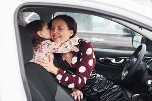 abraçando um ao outro. mãe com a filha dentro do automóvel moderno juntos foto