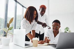 usando o mesmo laptop para o projeto. grupo de empresários afro-americanos trabalhando juntos no escritório foto