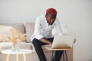 jovem afro-americano em roupas formais dentro de casa com laptop nas mãos foto
