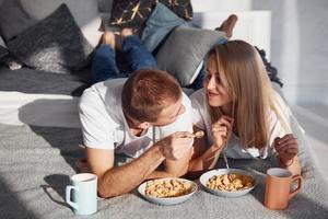 jovem casal adorável toma café da manhã em casa enquanto está deitado na cama foto