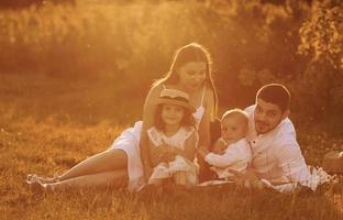 sentado na grama. pai, mãe com filha e filho passando o tempo livre ao ar livre no dia ensolarado do verão foto