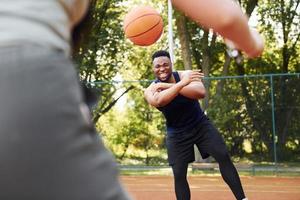 homem afro-americano com garota joga basquete na quadra ao ar livre foto