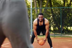 homem afro-americano com garota joga basquete na quadra ao ar livre foto