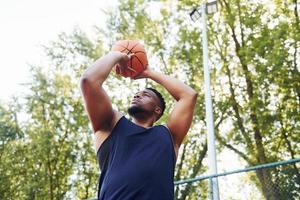 Tempo nublado. homem afro-americano joga basquete na quadra ao ar livre foto
