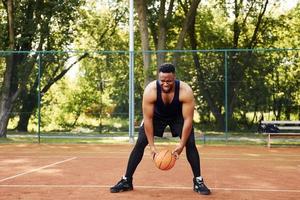 belas árvores verdes no fundo. homem afro-americano joga basquete na quadra ao ar livre foto