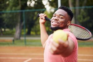 homem afro-americano de camisa rosa joga tênis na quadra ao ar livre foto