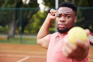 homem afro-americano de camisa rosa joga tênis na quadra ao ar livre foto