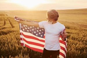 segurando a bandeira dos eua nas mãos. homem estiloso sênior patriótico com cabelos grisalhos e barba no campo agrícola foto