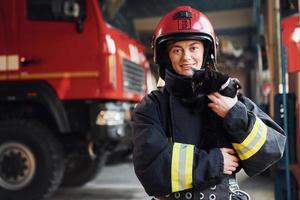lindo gato preto. bombeira em uniforme de proteção em pé perto de caminhão foto