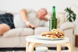 hambúrgueres e cerveja. homem deitado no sofá. homem engraçado com excesso de peso em roupas casuais está dentro de casa foto