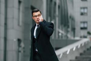 falando por telefone. empresário de terno preto e gravata está ao ar livre na cidade foto