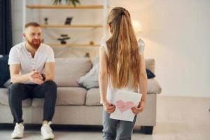 menina tem presente para o homem. pai com sua filha está em casa juntos foto