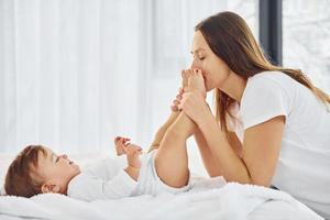 na cama branca. mãe com sua filha está dentro de casa juntos foto