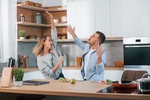 se divertindo. casal preparando comida em casa na cozinha moderna