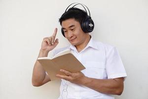 homem asiático lê livro e usa fone de ouvido para ouvir música suave para se concentrar na leitura. tenha ideia. conceito, tempo livre, passatempo, hobby, relaxe com música. foto