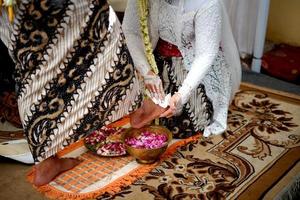 tradição de casamento na indonésia a noiva lava os pés do noivo foto