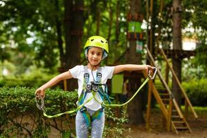 adorável menina aproveitando seu tempo na escalada do parque de aventura em um dia quente e ensolarado de verão. atividades de verão para crianças pequenas. criança se divertindo nas férias escolares. foto